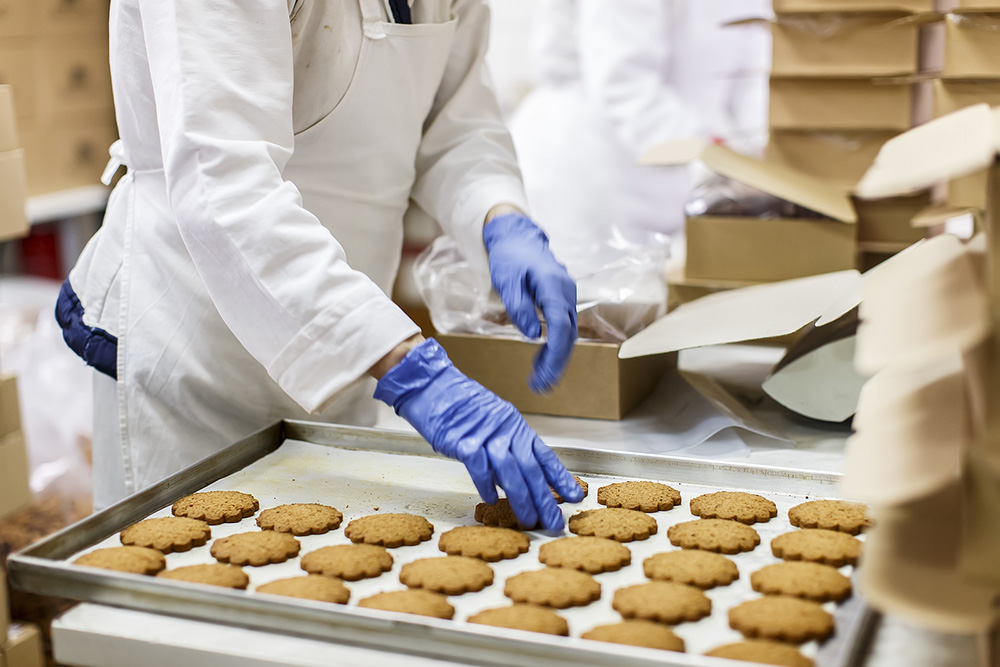 FSMA Compliance is a non-negotiable as a CPG Manufacturer worker checks cookies on a banking sheet on the food line.